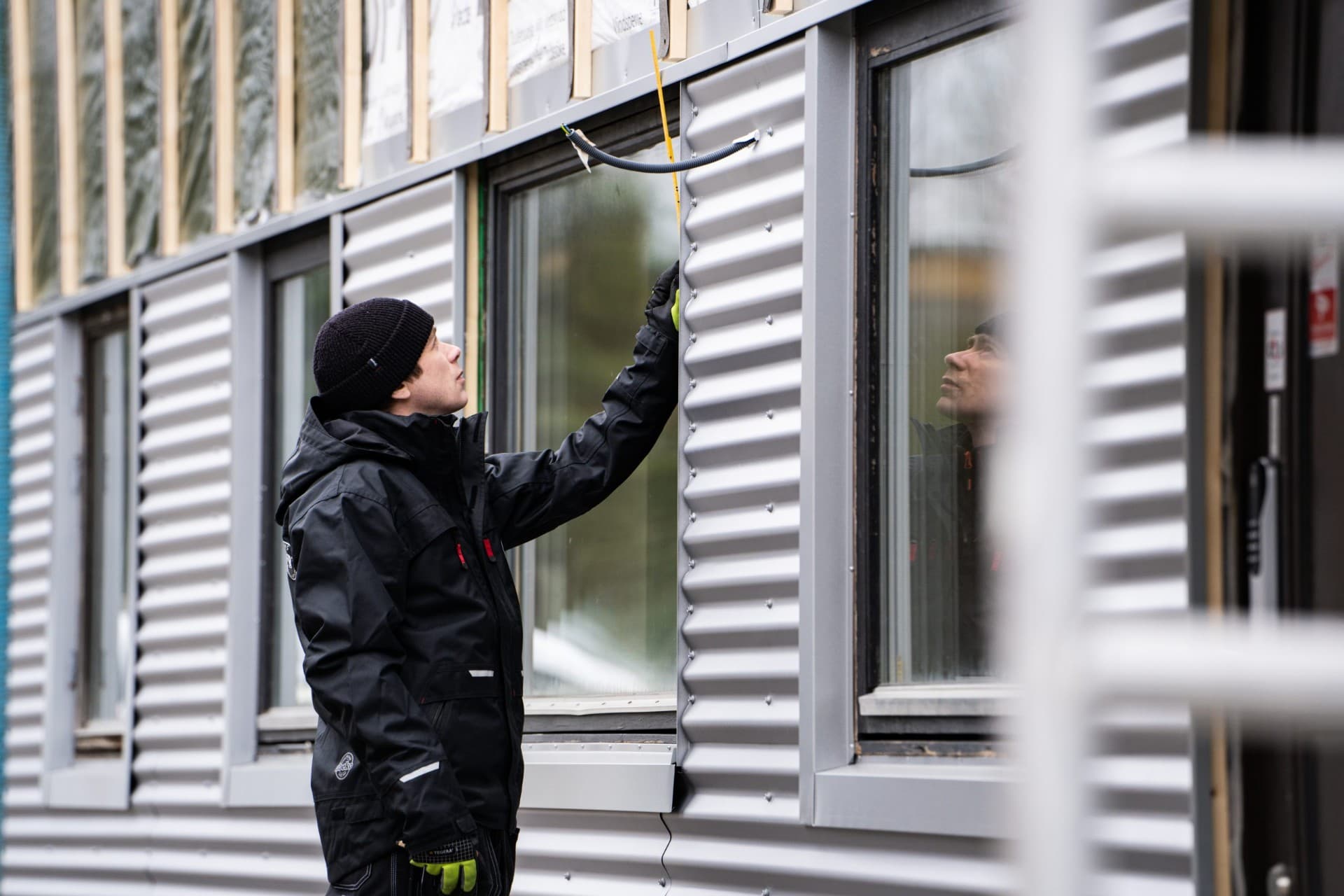 Plåtslagare monterar fasadplåt mellan fönster på byggnad