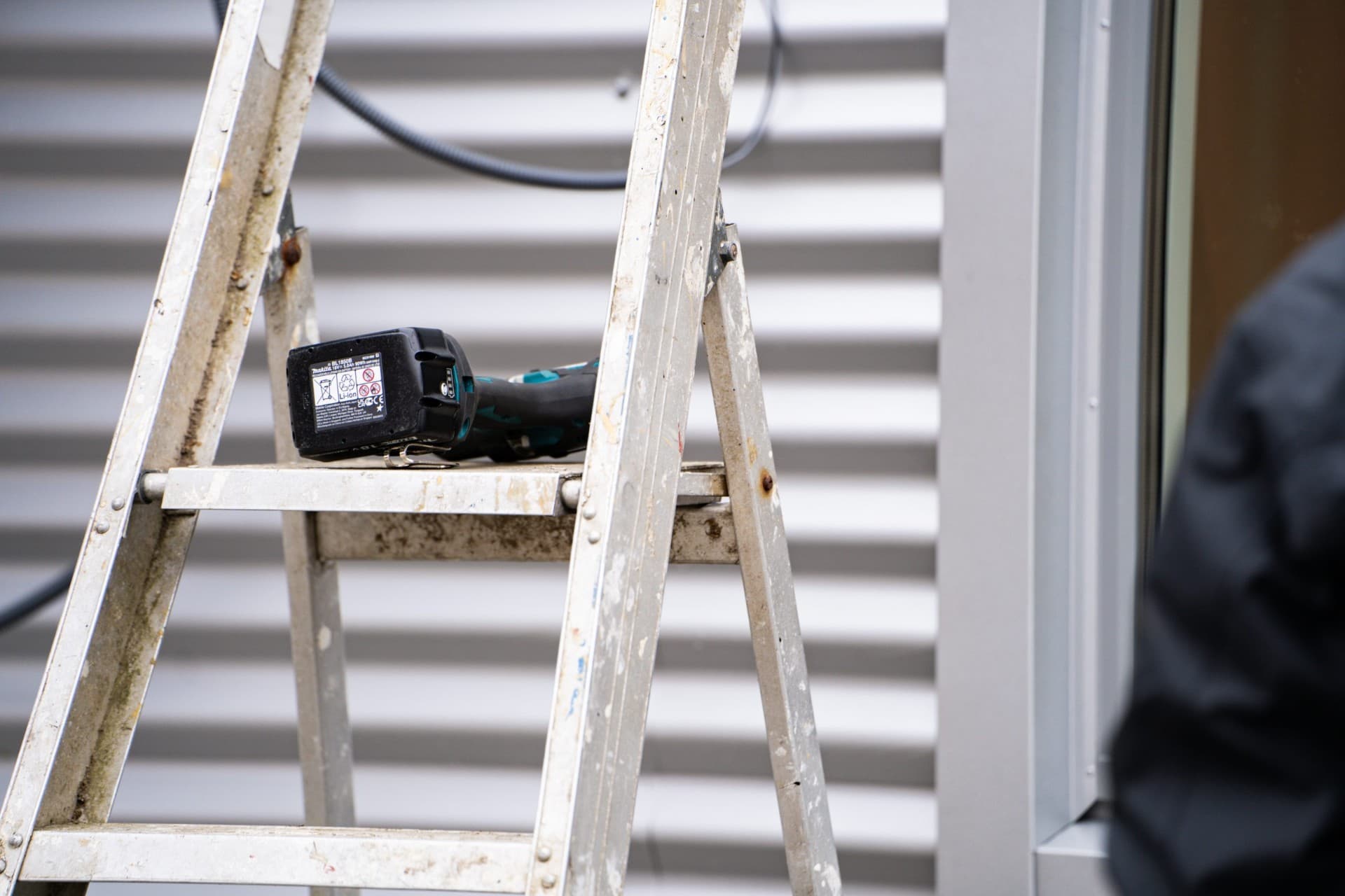 Makita borrmaskin på aluminiumstege framför plåtfasad